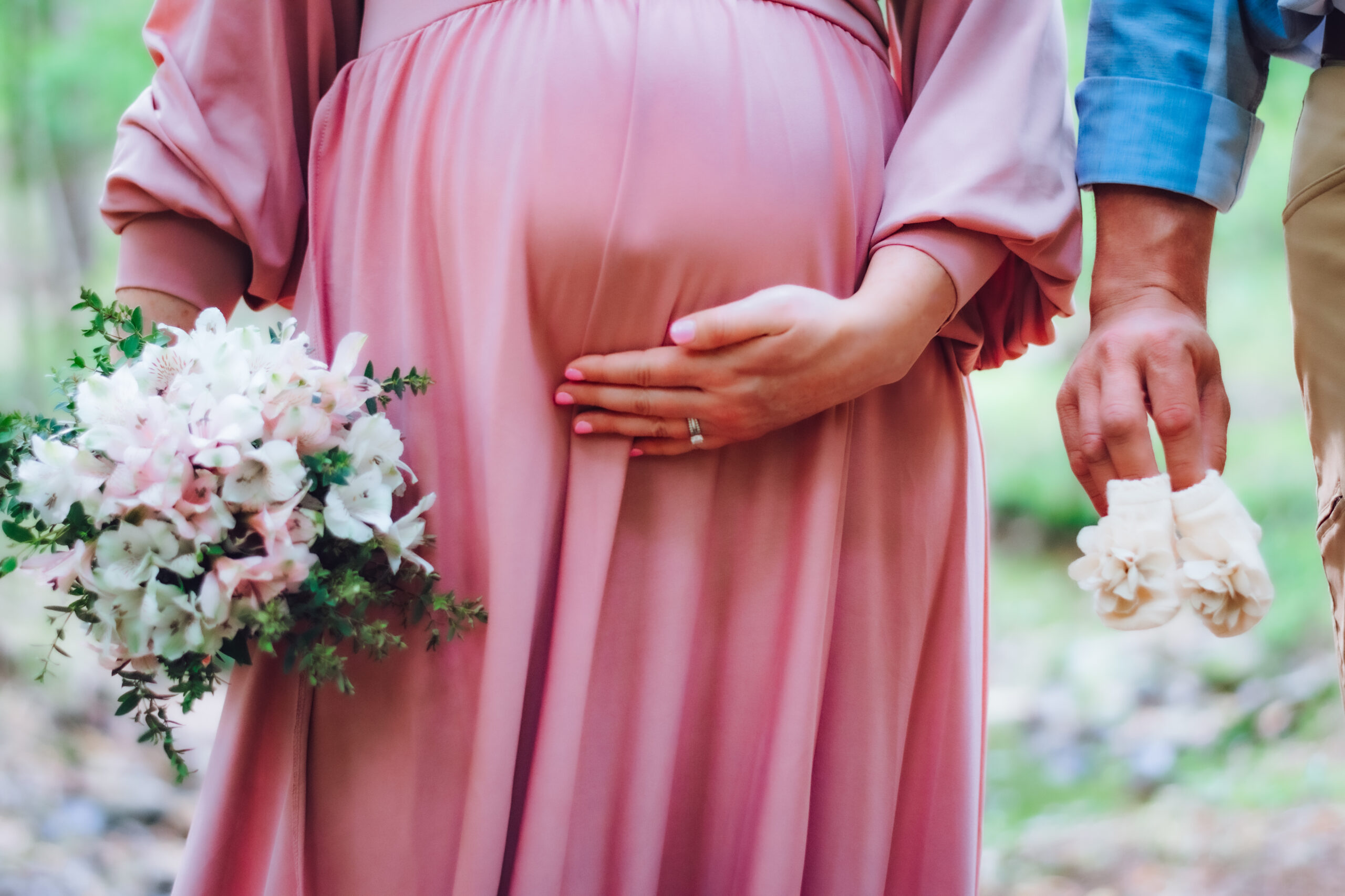 Expecting mama and daddy hold baby baby bump, floral arrangement and baby shoes in maternity photoshoot