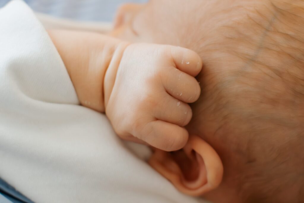 Baby's hand rests curled up next to his temple, new skin a little flaky, in this macro image taken during an in-home newborn session.