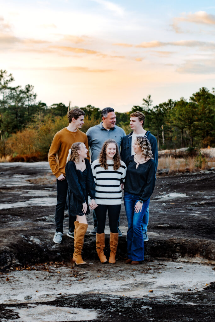 Family stands at different levels looking at each other and laughing during a family photo session during golden hour.