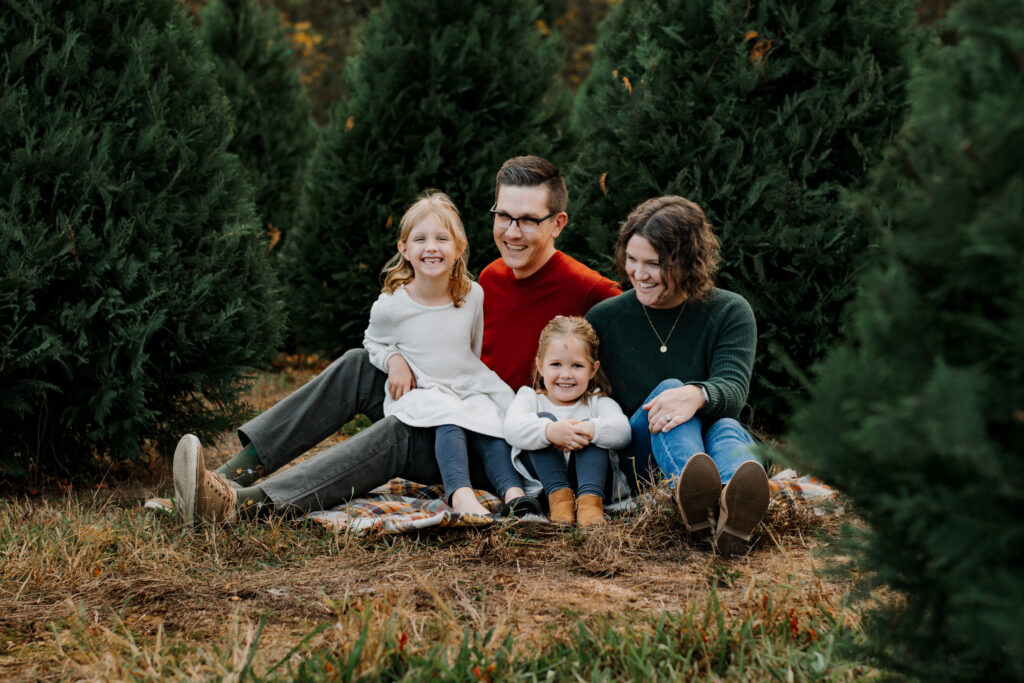 Family piled on a blanket at a Christmas tree farm