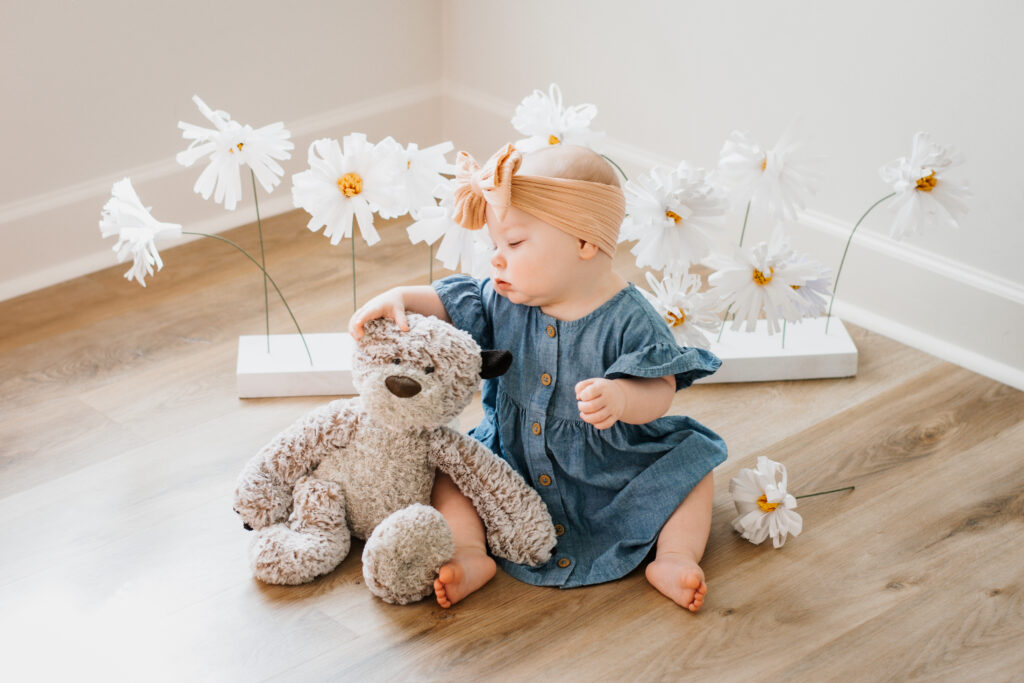 Girl and teddy bear in front of paper daisies during a milestone photoshoot