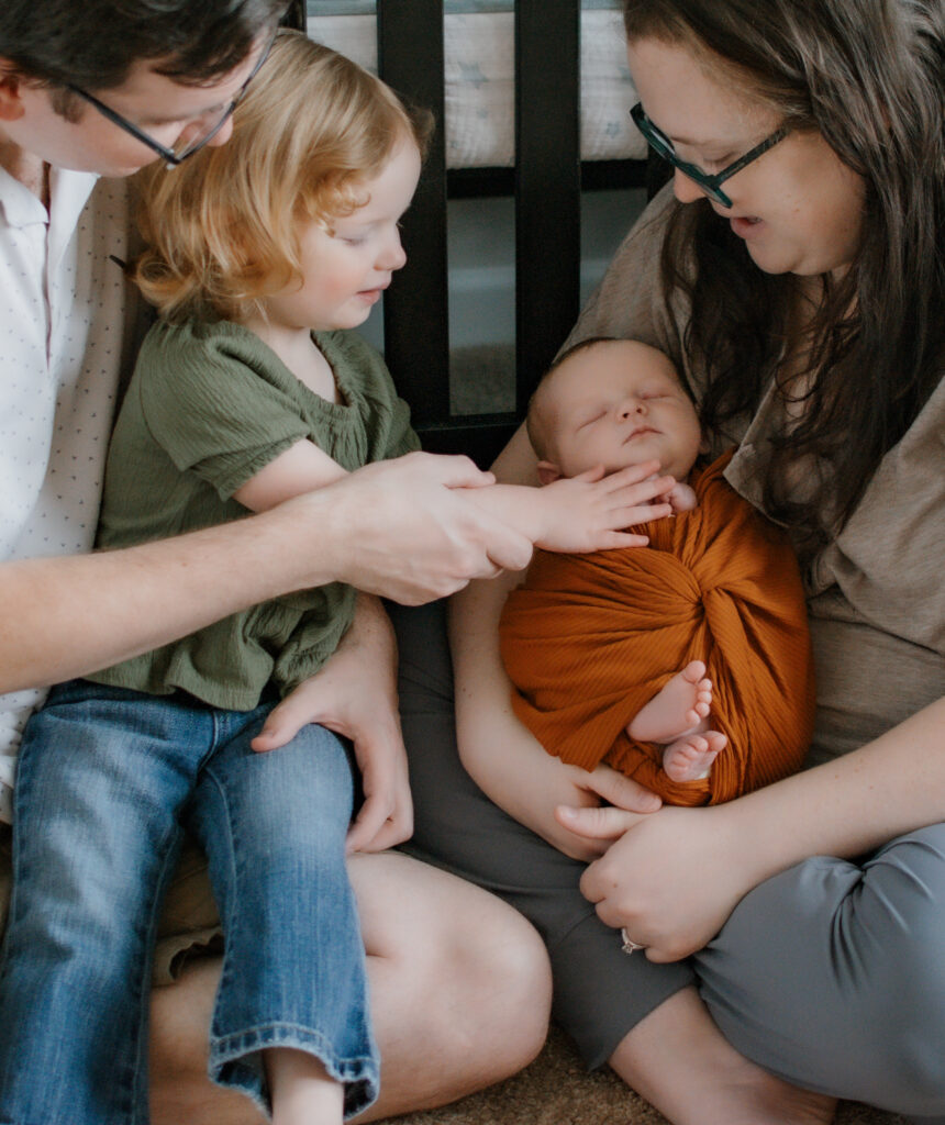 Dad helps guide his daughter's hand gently to touch the hand of her newborn brother during an in-home newborn session