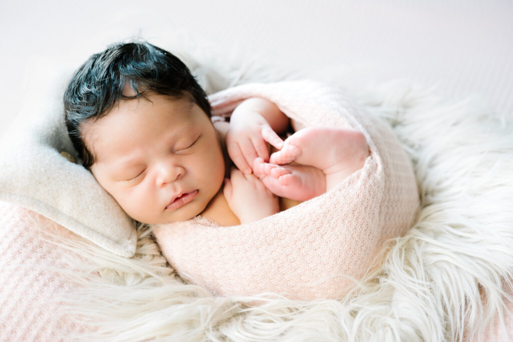 Newborn girl in egg pose wrapped and resting during her in-home newborn photo session.