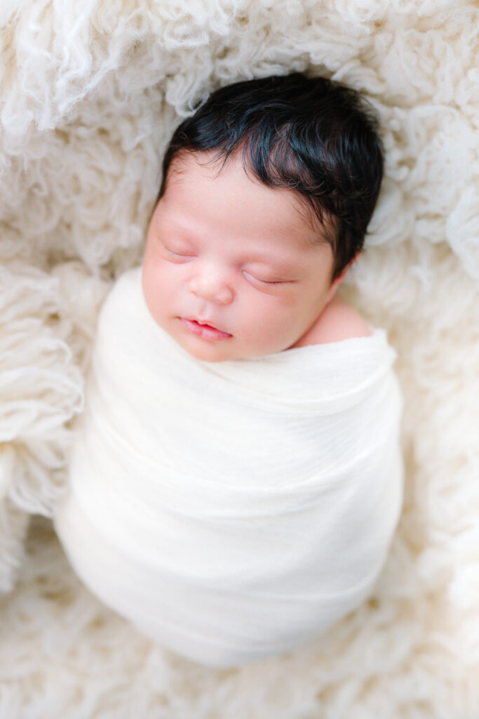 newborn posing on white wool flokati during in-home newborn shoot