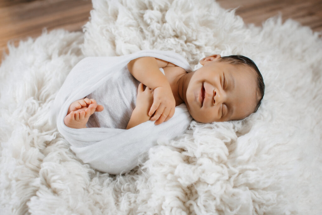 smiling newborn on white fur rug during in-home photo session
