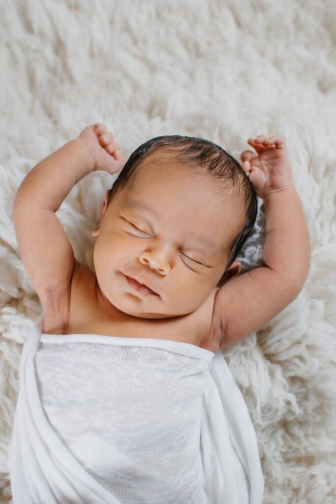 newborn photo of baby asleep grinning with arms above head