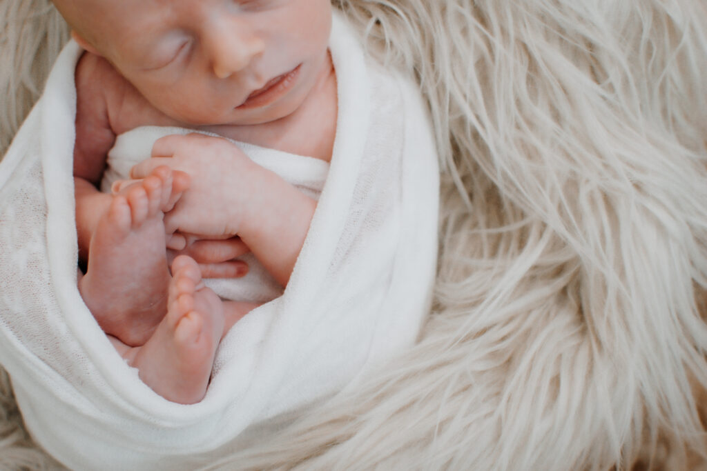 newborn boy asleep in egg pose wrapped in cream swaddle