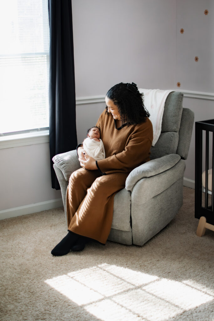 Mom cradles newborn in nursery chair in in-home lifestyle photo session in Atlanta