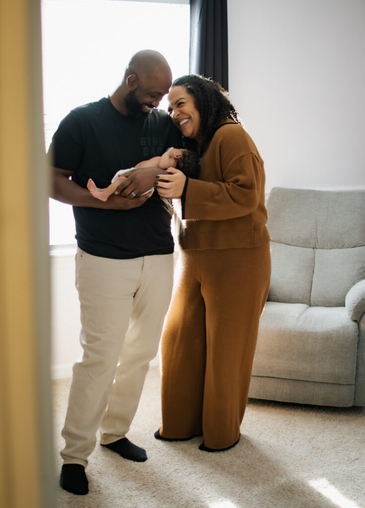 Mom and dad laugh holding their baby during a newborn session in Lawrenceville, Georgia