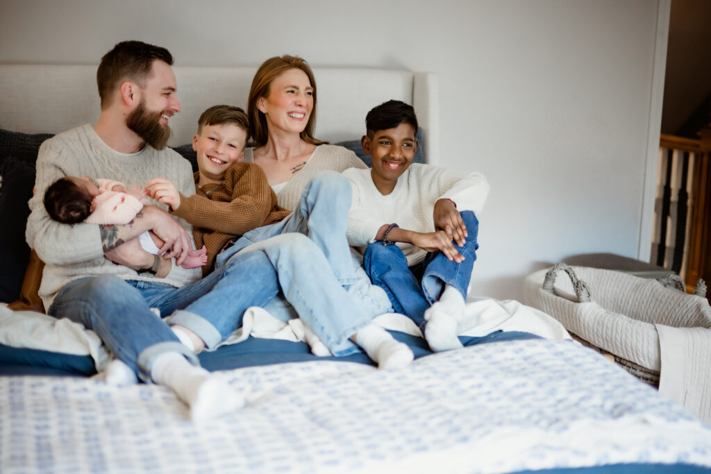 Family laughing on bed with newborn