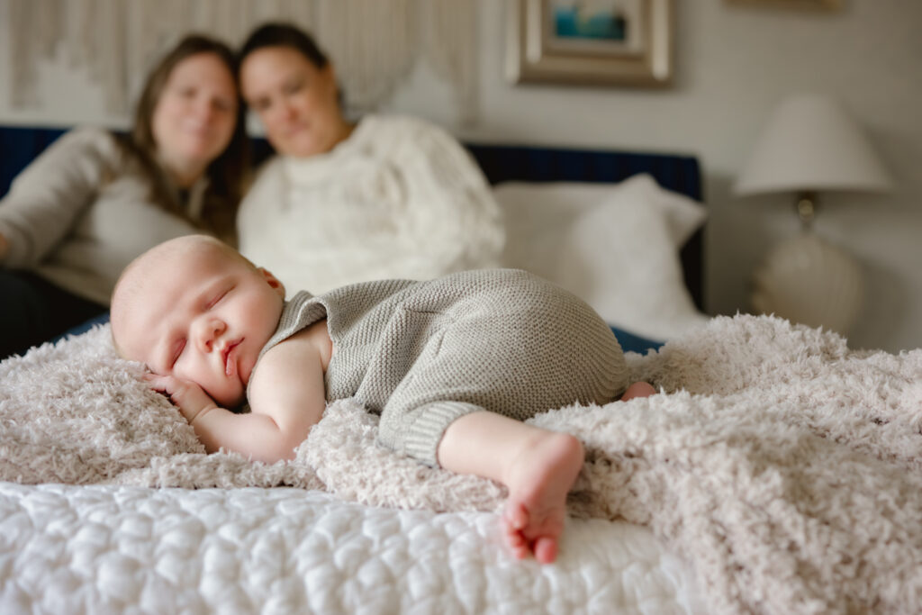 Moms put heads together and grin at sleeping baby during in-home newborn session