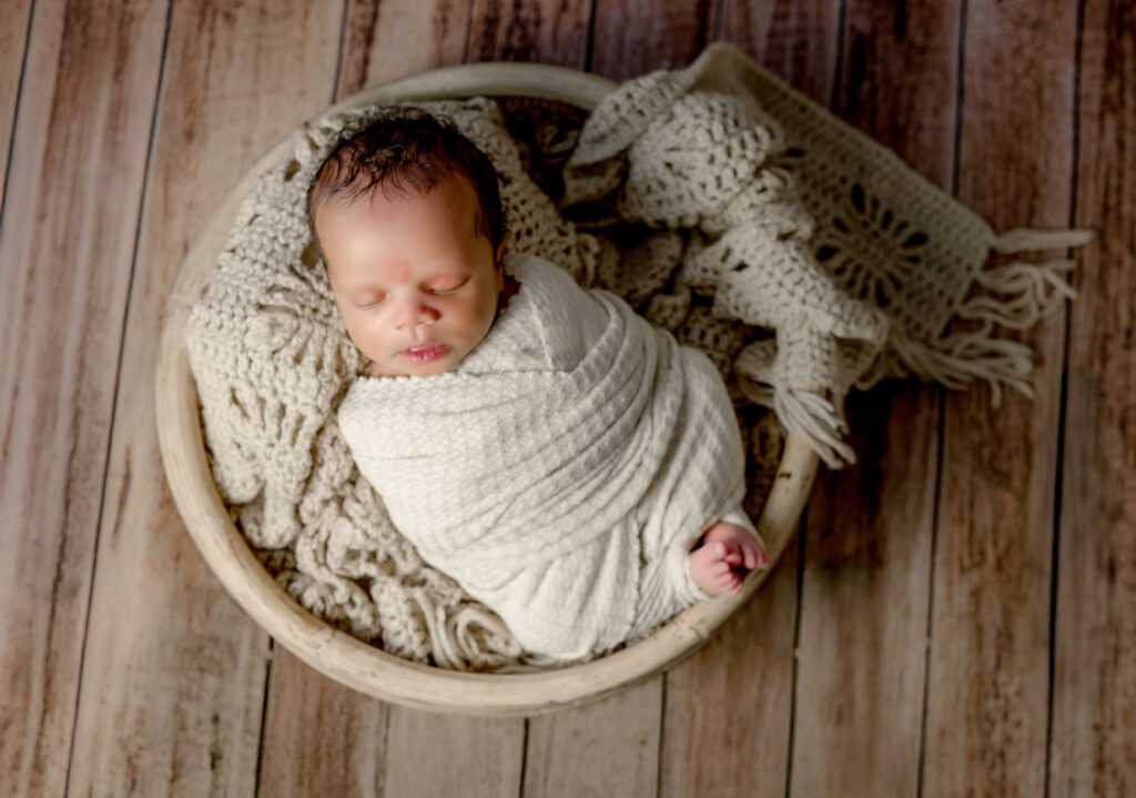 Baby sleeping posed in a bowl on a wood floor during a newborn session