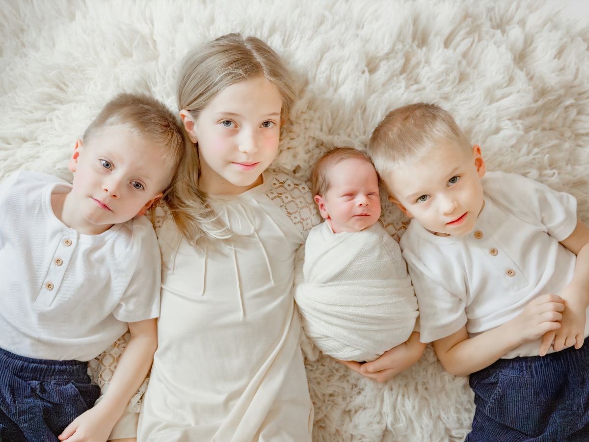 Image of siblings with newborn brother on white fur rug