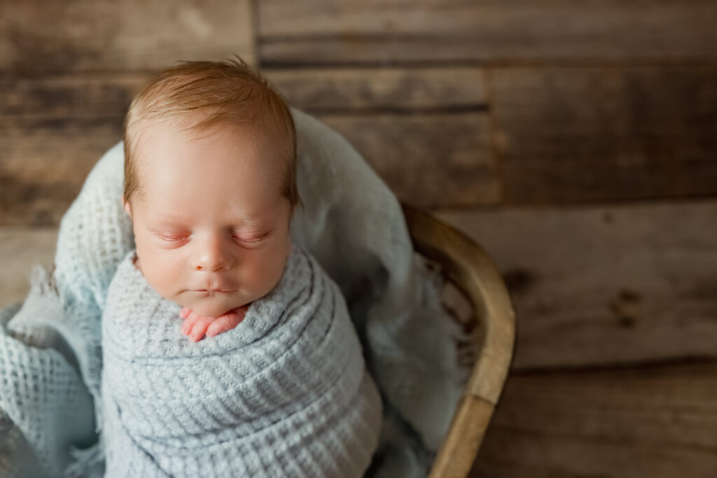 Sleeping newborn baby in blue wrap posed in basket