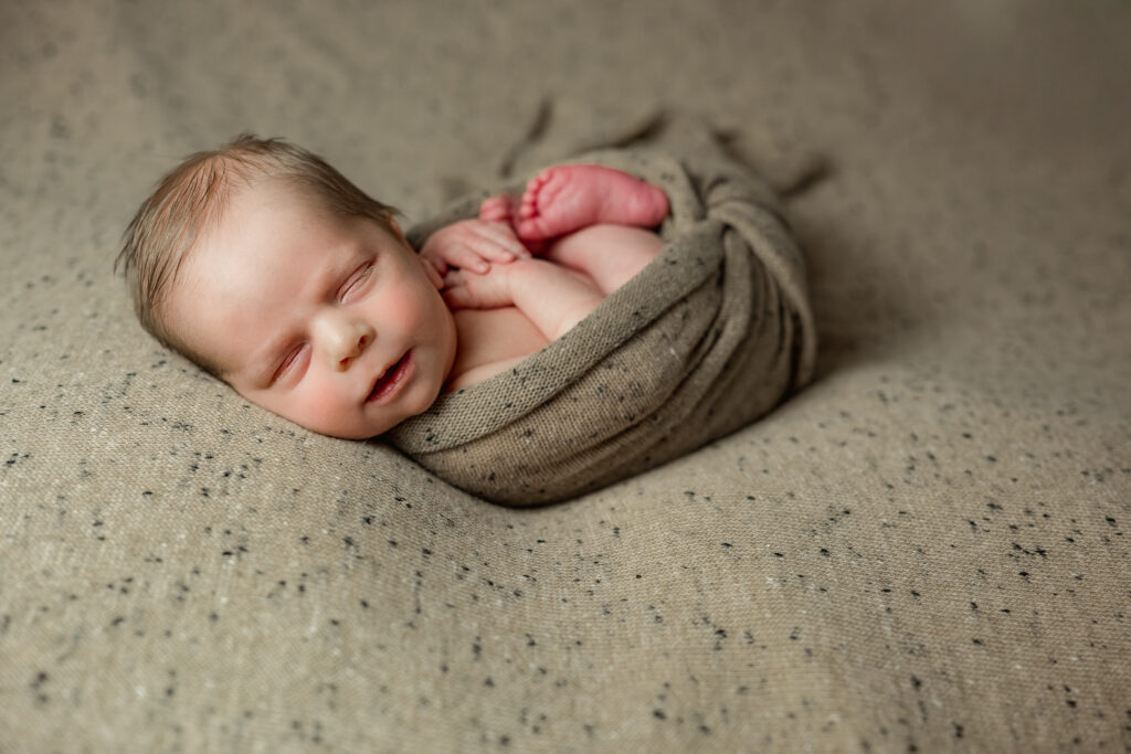 Smiling newborn wrapped in neutral speckled wrap