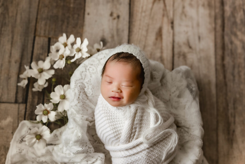 smiling newborn posed in bowl with florals during in-home session