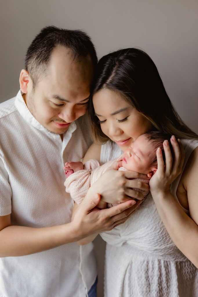 couple holds newborn and gazes down at her during in-home session in Lawrenceville, Georgia