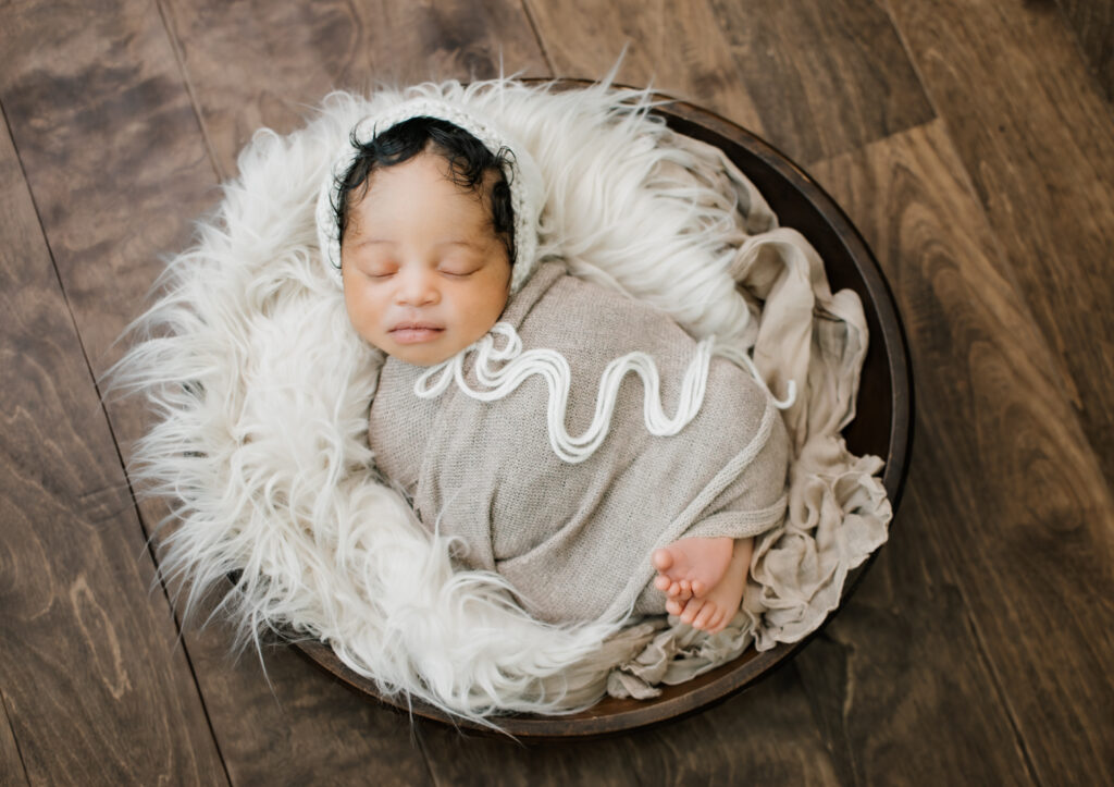 Newborn boy sleeps peacefully in the neutral coordinated set in a bowl with fur layer during his Decatur, Georgia newborn photography session. 