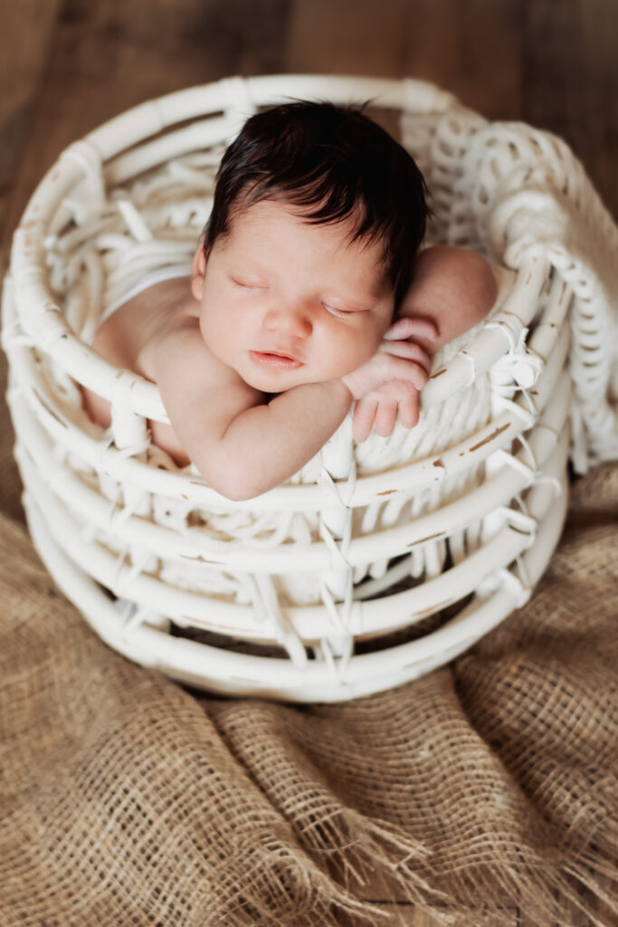 Bab girl rests in a white basket, her arms draped over the side, during an in-home newborn session in Peachtree Corners. 