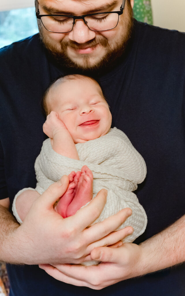 Dad holds smiling newborn during Tucker, Georgia in-home photo session