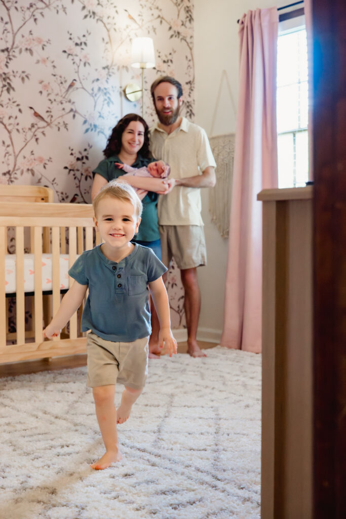 Toddler smiles and runs toward camera during Tucker, Georgia in-home newborn session