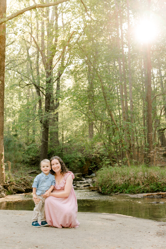 mom kneels with son creekside during Atlanta Georgia materntiy session