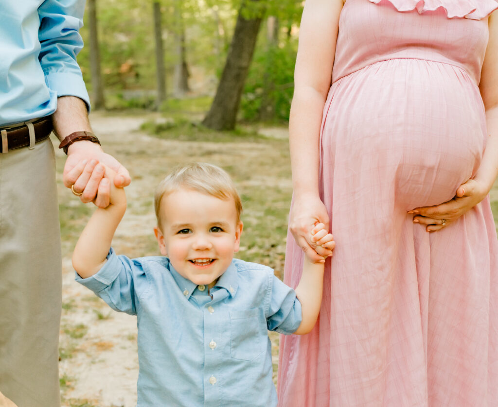 Little boy hold mom and dad's hand during maternity session at Stone Mountain, Georgia