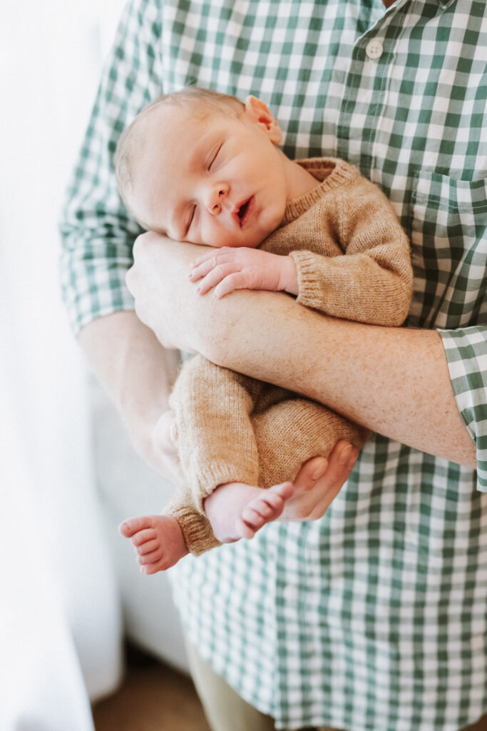 Dad holds sleeping son against his check, hands curled together, during an in-home newborn session in Atlanta, Georgia.